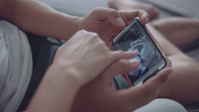 一对年轻的怀孕夫妇在智能手机上看超声波图像视频下载