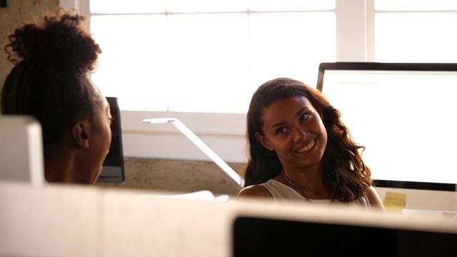 微笑的女商人坐在设计室的工作台上与同事讨论视频素材