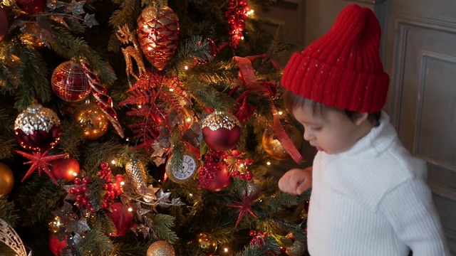 穿着白色针织毛衣的孩子站在挂着花环的圣诞树前视频下载