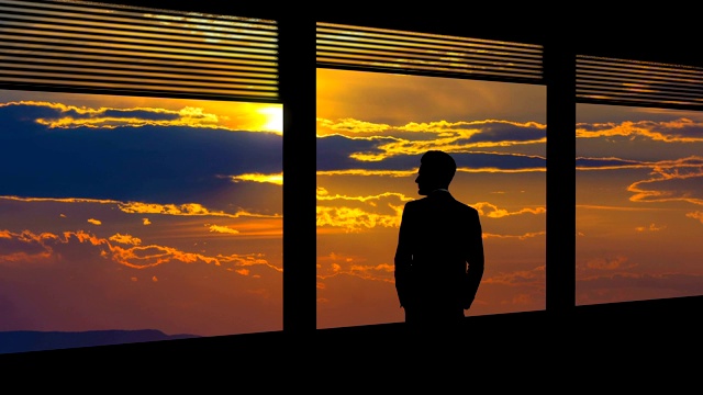 在夕阳的背景下，那个商人站在靠近窗户的地方。时间流逝视频素材
