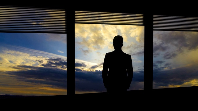 那个男人站在一扇窗户旁边，背景是云流。时间流逝视频素材