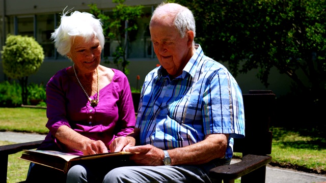 正面的观点积极的白人老年夫妇看相册在花园里的疗养院4k视频素材