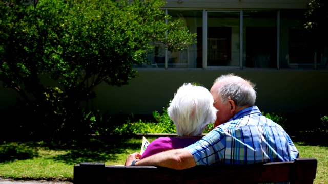 后视图积极的白人老年夫妇看相册在花园里的疗养院4k视频下载