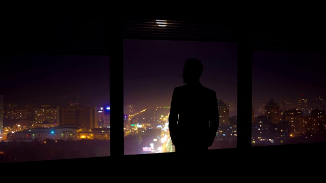 在夜色中的城市背景中，那个男人站在窗边。时间流逝视频素材