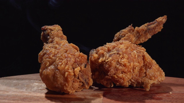 鸡翅和鸡腿的炸鸡与热烟从左到右的黑色背景锅视频下载