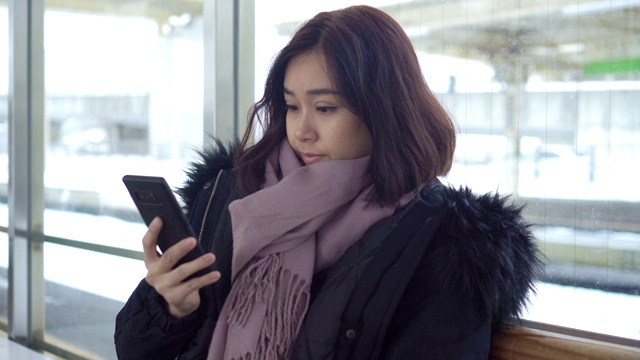 一个拿着智能手机在火车站等车的女人。视频素材