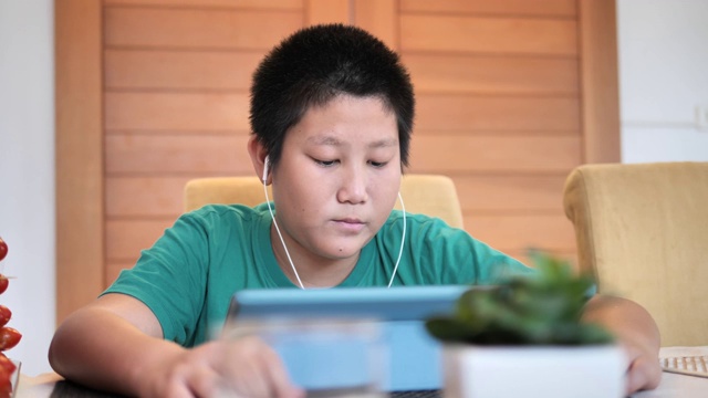 快乐的青春期前亚洲男孩用耳机在家里用平板电脑看电影。视频下载
