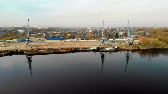三个工业起重机反射在河港的水中，驳船和拖船以城市为背景视频素材