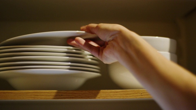 一个白人妇女的手把不同大小的碗放在一个打开的厨房碗柜里，然后关上门视频下载