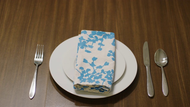 一个白人妇女在一个白色餐盘的两边分别放上叉子、刀和勺子，上面放上一个白色沙拉盘，然后在盘子上放上一块五颜六色的花布餐巾视频素材