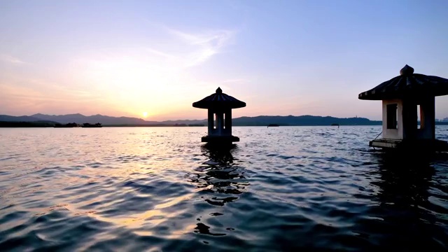 中国杭州西湖美丽的夕阳景观，橘色的黄昏天空和宁静的水与湖中的传统亭台楼阁，闪烁的涟漪，4k电影，慢镜头。视频素材