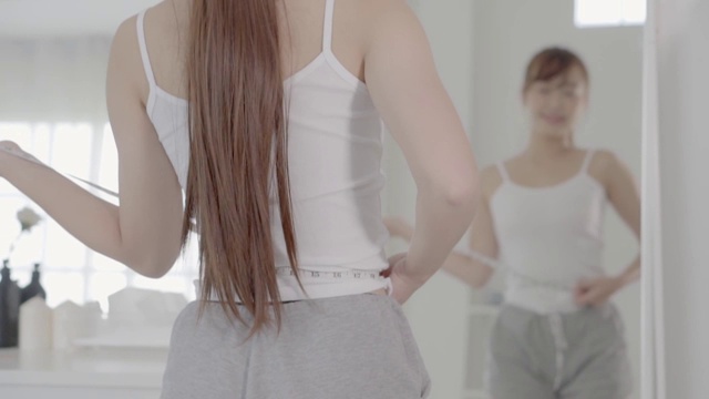 美丽肖像年轻的亚洲身材女人节食瘦体形看镜子与腰围测量腰围和腹部，亚洲女孩与苗条反射在镜子与测量尺，减肥和生活方式的概念。视频素材