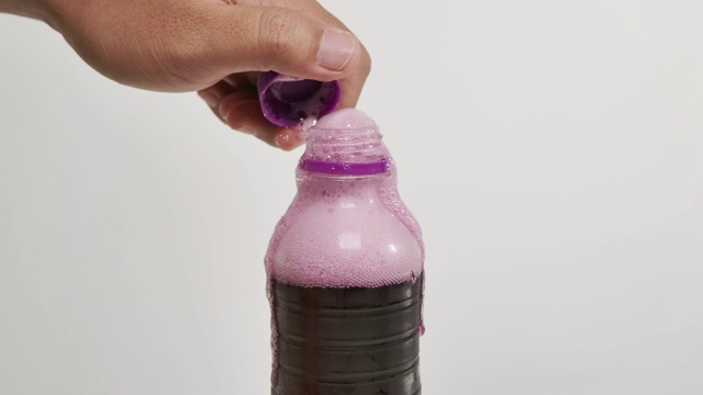 一个男人打开一个气泡葡萄紫色的软饮瓶盖的特写白色的背景。视频素材