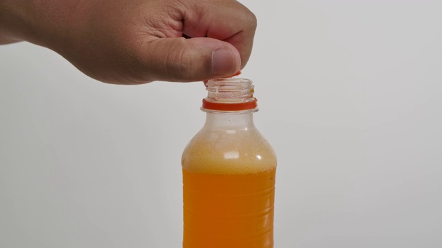 一个男人打开一个瓶盖上的橙色气泡饮料在白色的背景。视频素材