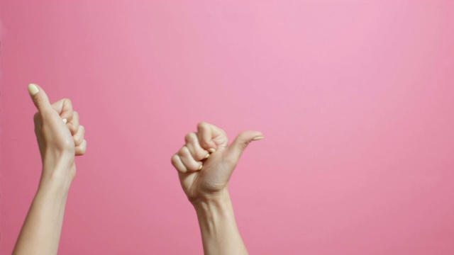 年轻女子的双手竖起大拇指，女孩在粉红色的工作室背景上展示手势课的广告视频下载
