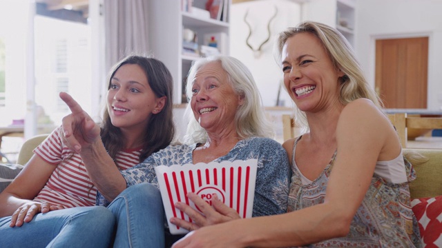 母亲与成年女儿和十几岁的孙女在家里的沙发上吃爆米花看电影视频素材