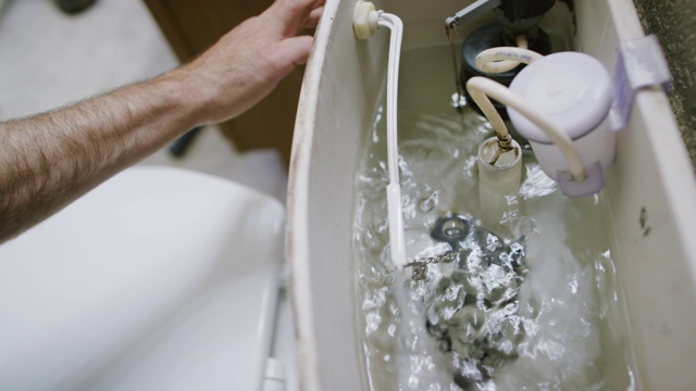 在室内家庭浴室里，白种人修理工通过向下推下冲厕杠杆，将马桶水箱盖移开来冲厕视频下载