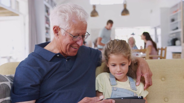 祖父和孙女坐在沙发上，在家里使用数字平板电脑视频素材