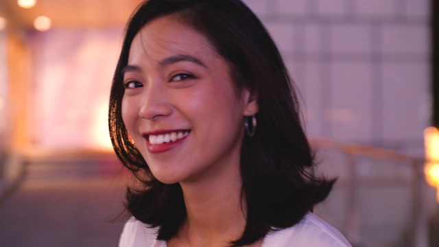 可爱的年轻亚洲女人微笑在相机在夏城晚上，4k视频素材