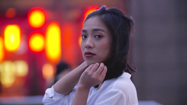 侧面的漂亮的年轻亚洲女人看镜头微笑在城市视频素材