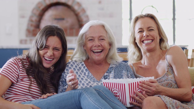 母亲与成年女儿和十几岁的孙女在家里的沙发上吃爆米花看电影视频素材
