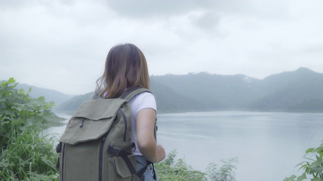徒步女背包客徒步冒险感觉自由行走在森林附近的湖在雨天。生活方式女性旅游放松的概念。视频素材