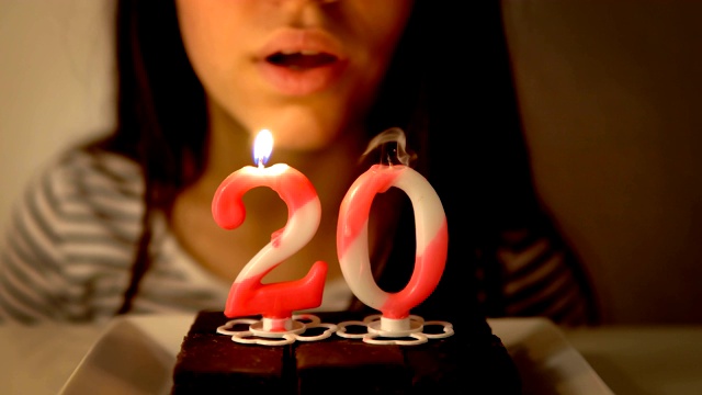 快乐的少女庆祝她的20岁生日和吹蜡烛自制烤蛋糕，室内视频下载