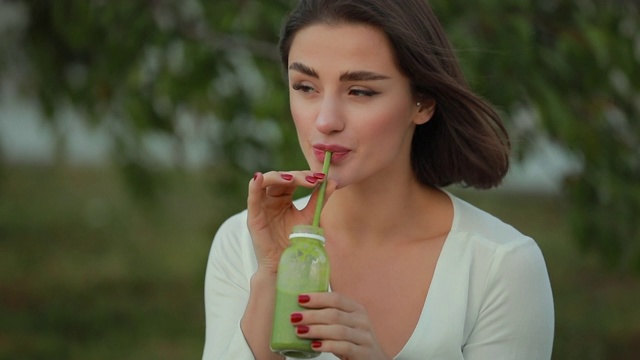 美丽的女人在户外喝绿色奶昔，排毒概念视频素材