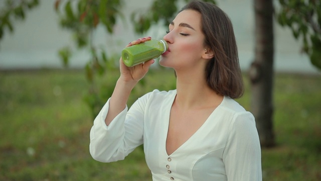 美丽的女人在户外喝绿色冰沙视频素材