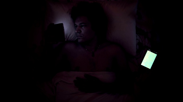 男人在床上用手机看平板电脑。视频下载