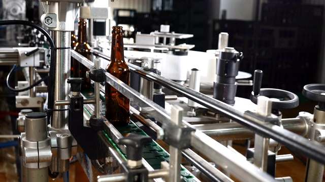啤酒厂啤酒装瓶工艺线。工厂生产线上的棕色空瓶子。玻璃瓶厂传送带上移动的瓶子。手把瓶子放在传送带上。4 k视频素材