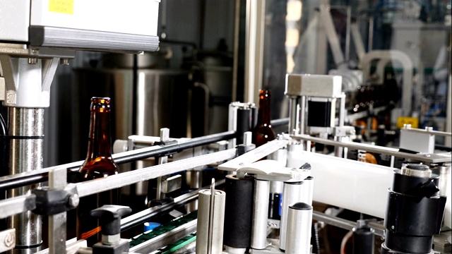 食品行业。自动啤酒装瓶生产线。应用标签。啤酒瓶标签贴标机。空瓶子在啤酒厂的技术线上移动。4 k视频素材