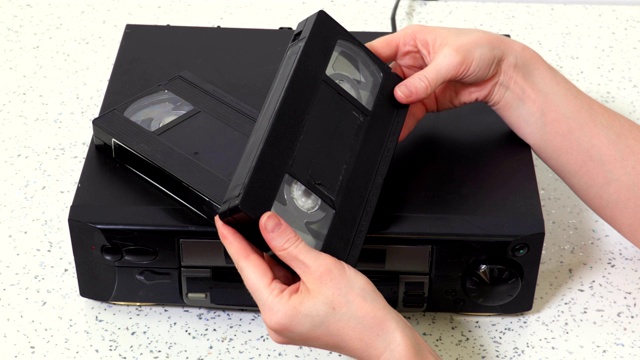 女人在桌子上的VCR播放器旁边选择VHS磁带视频下载