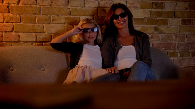 特写拍摄的年轻白人女性和她的小女儿看一个动作片电视在家里的3D眼镜视频下载