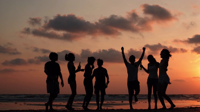 剪影亚洲青少年群舞和饮料一起在海滩夏季日落背景。年轻的亚洲快乐的情感和周年庆典。4K分辨率和慢镜头。视频下载