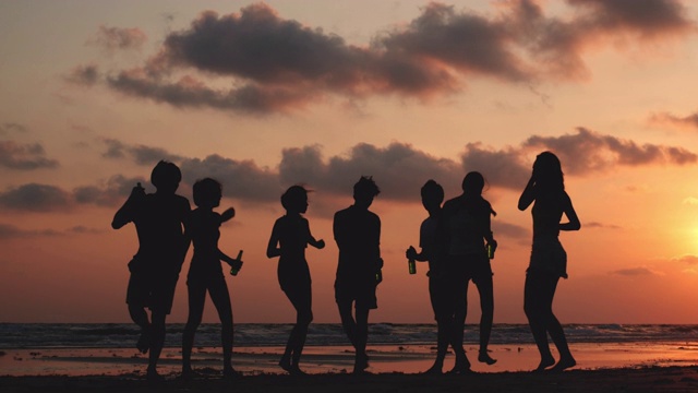 剪影亚洲青少年群舞和饮料一起在海滩夏季日落背景。年轻的亚洲快乐的情感和周年庆典。4K分辨率和慢镜头。视频素材