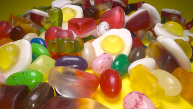 滑过一堆美味多彩的嚼糖背景。黄色背景上五颜六色的糖果视频下载