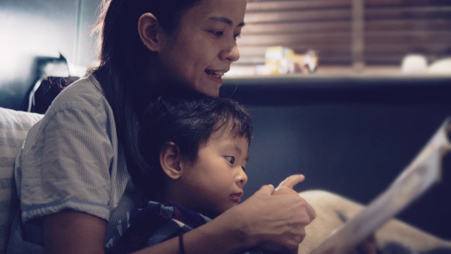 亚洲母亲和儿子晚上在床上看书。视频素材