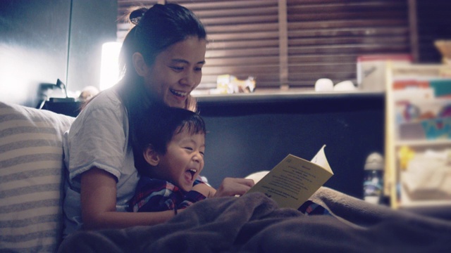 亚洲母亲和儿子晚上在床上看书。视频下载