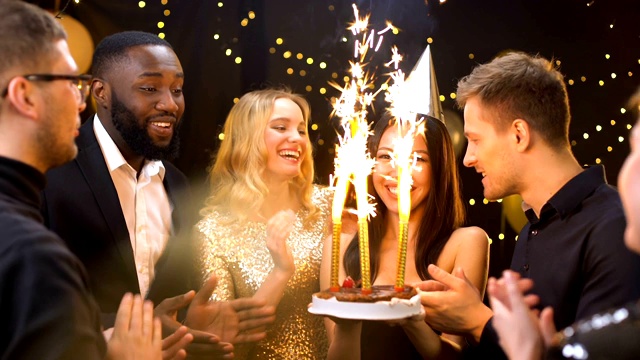 朋友祝贺漂亮的女人在派对帽子拿着生日蛋糕烟花视频素材