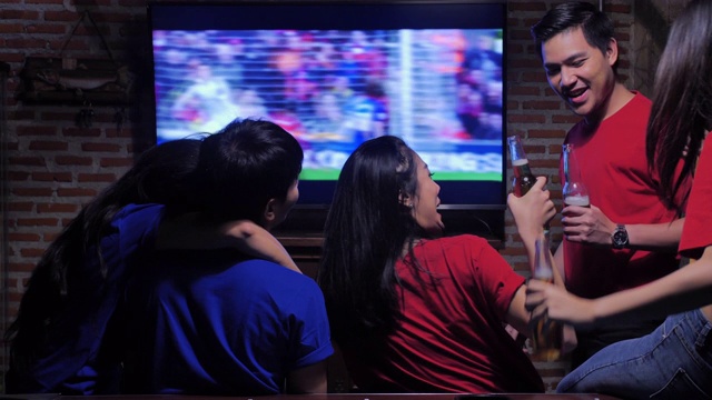 不同的亚洲朋友群在体育酒吧看电视。他们队进了一球，赢了。兴奋的朋友一边看足球比赛一边在酒吧喝啤酒。当他们喜欢的球队得分时，他们都欢呼。快乐的年轻人。视频素材