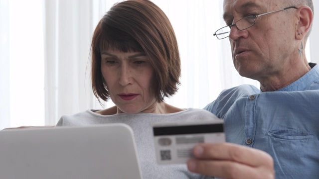 一对老年夫妇在家里用笔记本电脑网购视频素材