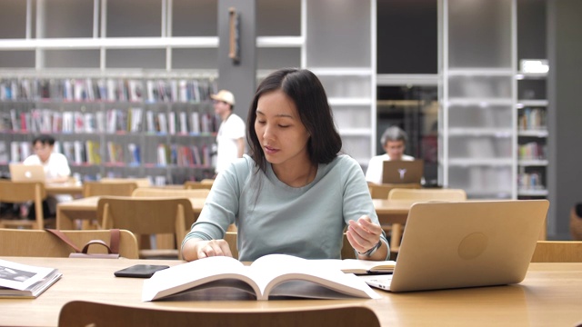 亚洲女学生使用智能手机进行图书馆教育，阅读书籍和做笔记视频下载