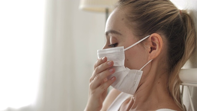 妇女咳嗽，带着口罩躺在家里的床上视频素材