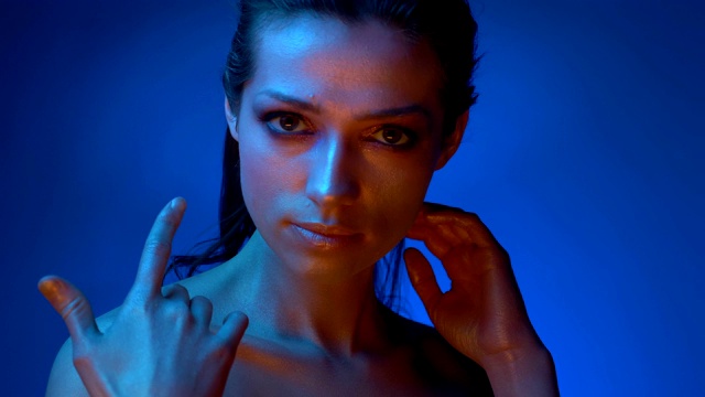 在蓝色霓虹灯下，一名化妆闪亮的模特摸着锁骨，目不转睛地看着镜头。视频下载