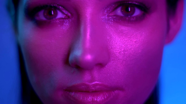 宇宙的时尚模特，在紫色的霓虹灯下，带着闪闪发光的妆容，在工作室里平静地看着镜头。视频下载