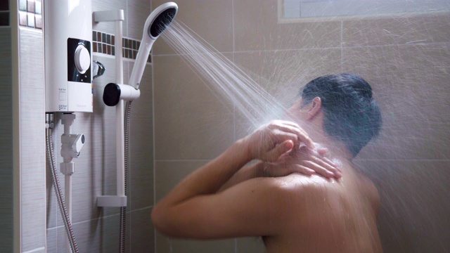 年轻的亚洲男人在浴室里用淋浴洗澡，充满新鲜感。视频素材