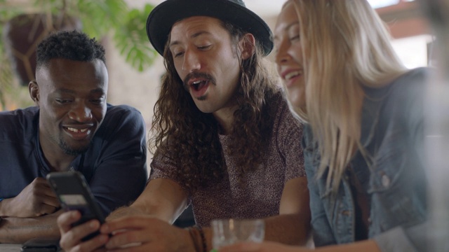 在奥斯丁酒吧的欢乐时光里，三个时髦的年轻朋友一边看着手机一边谈笑风生。视频素材