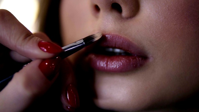 极其近距离的镜头，化妆师用唇膏刷在嘴唇上的年轻女子。为彩妆模特加工唇彩视频素材