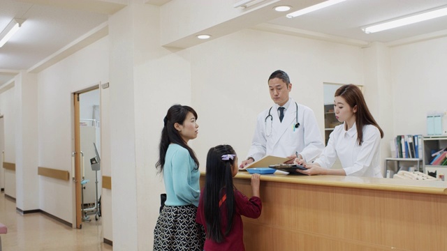 医生和护士在医生办公室的接待处与母亲和女儿交谈视频下载